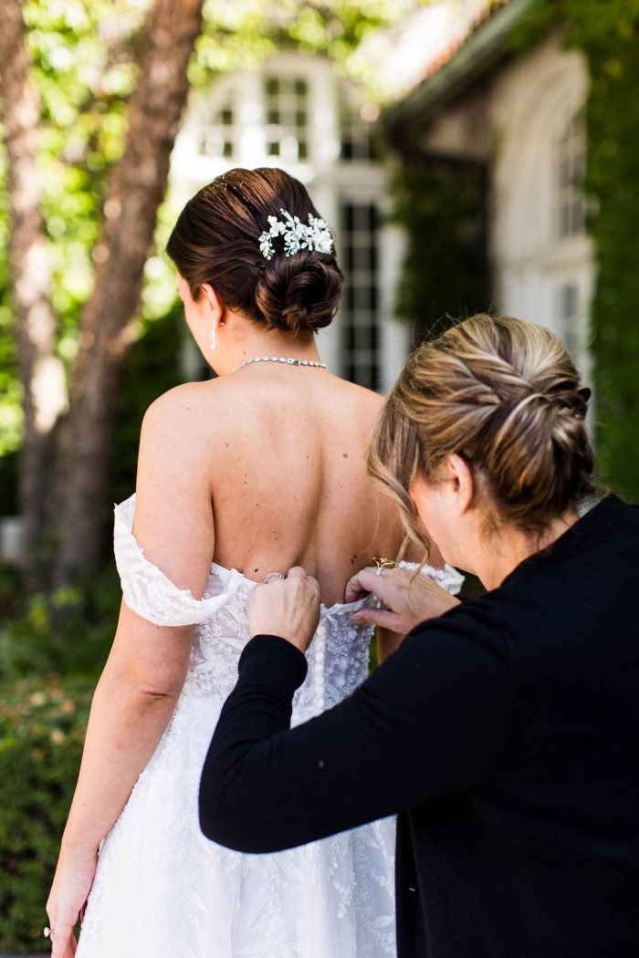 Bride wearing Oriana by Maggie Sottero while she gets buttoned up by her mother