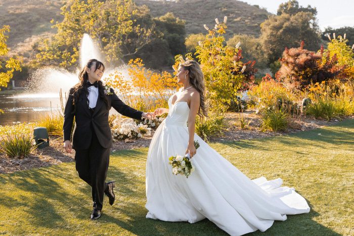 Bride wearing Maggie Sottero Derrick wedding dress walking hand in hand with partner during outdoor garden wedding