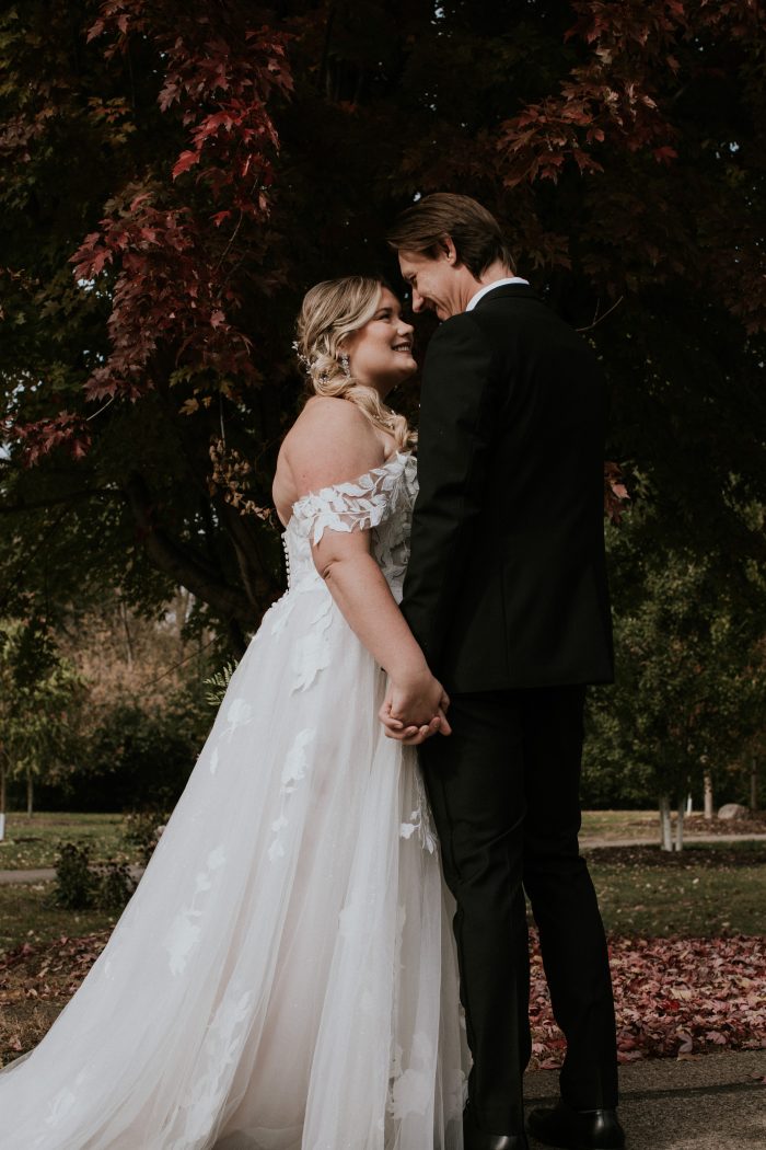 Blonde Bride In Off-The-Shoulder Wedding Dress Called Hattie Lane Lynette By Rebecca Ingram With Groom In Black Suit