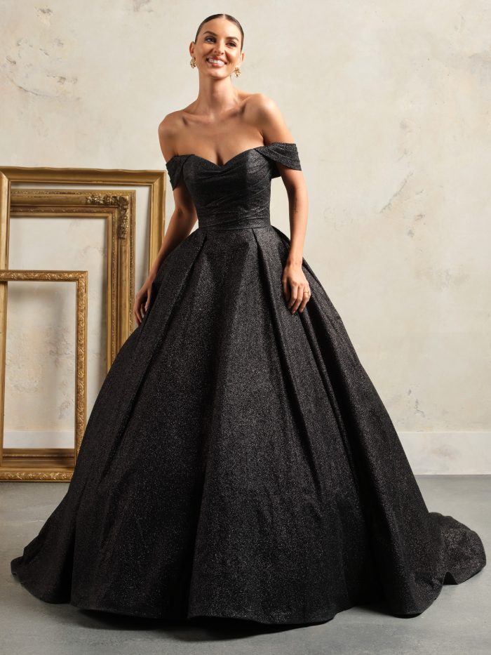 Anniston by Maggie Sottero, a glamorous black ballgown wedding dress with off-the-shoulder straps, sweetheart neckline, and shimmering fabric designed to sparkle.