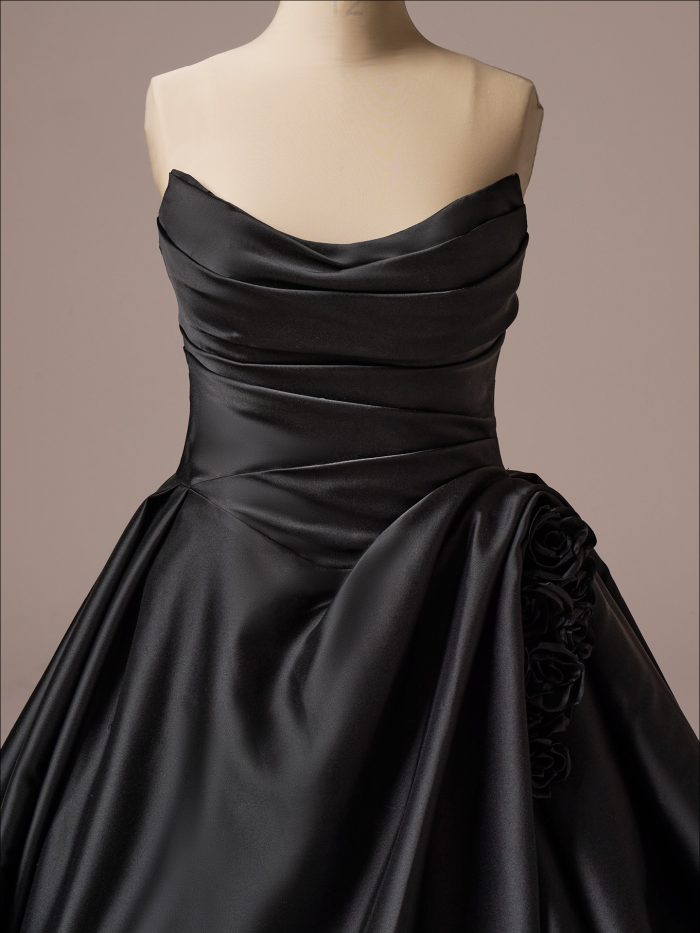 Close-up of Antoinette black ballgown wedding dress bodice with draped satin neckline, ruched detailing, and side floral appliqué accent.