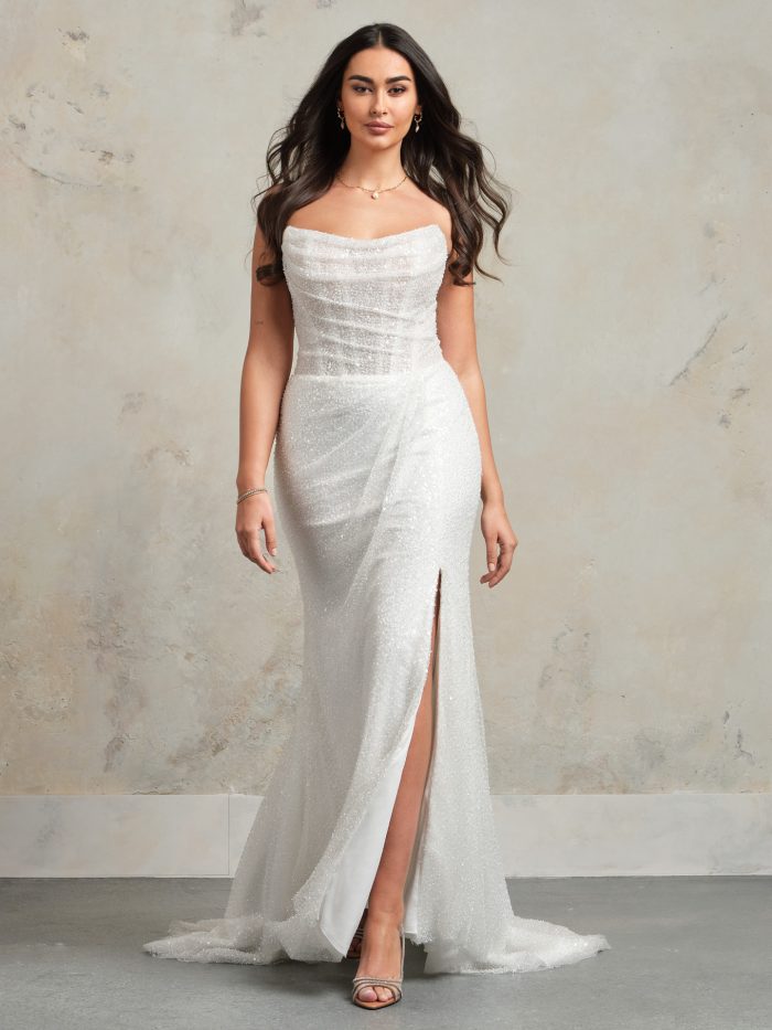 Ashley sheath wedding dress with a draped beaded bodice, strapless neckline, thigh-high slit, and sparkling layered skirt by Maggie Sottero.