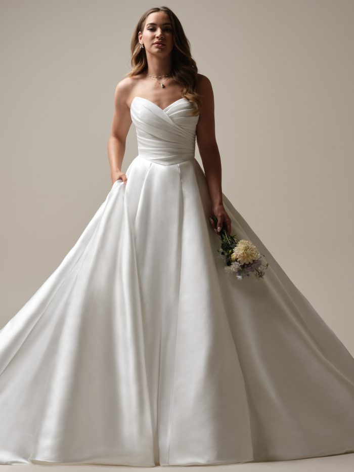 Bride in strapless Mikado ball gown wedding dress with sweetheart neckline, ruched bodice, and full skirt with hidden pockets, styled with simple jewelry.