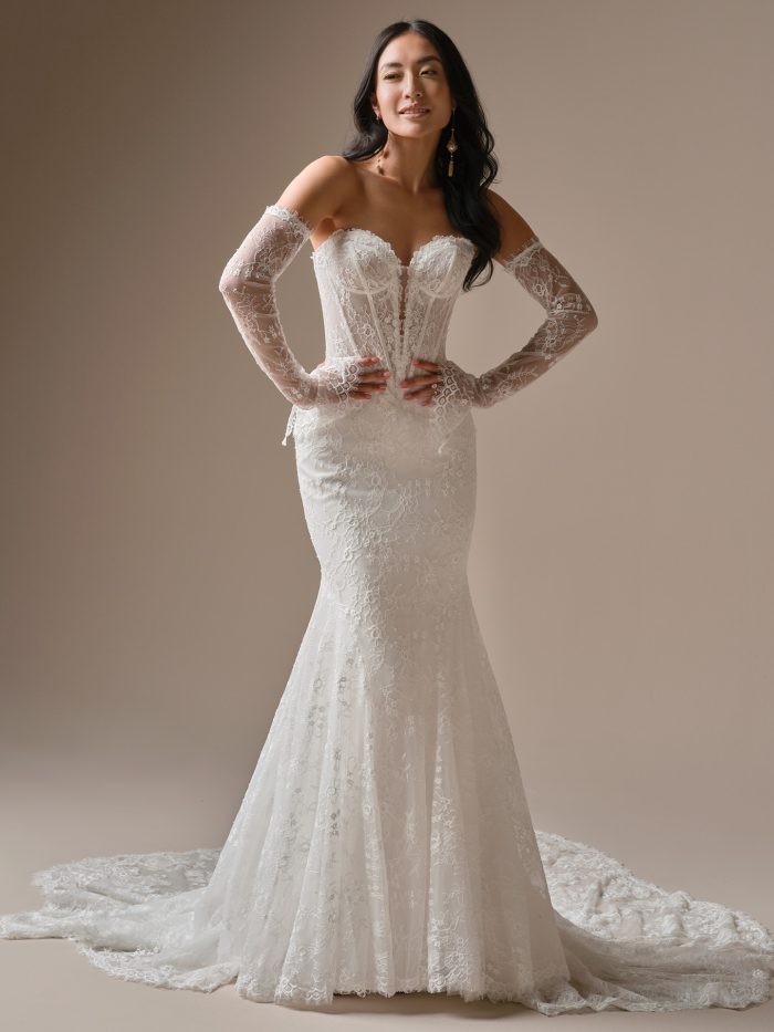 Bride wearing the Bellevue fit-and-flare wedding dress by Maggie Sottero, featuring an exposed corset bodice, off-the-shoulder illusion lace sleeves, 3-D floral lace, and a dramatic lace train.
