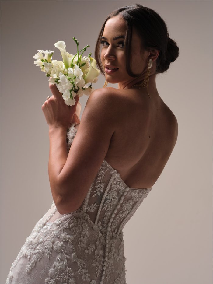 Close up of the Benjie Royale wedding dress showing the beaded lace bodice, illusion corset detailing, and covered button back as the bride holds a small bouquet.