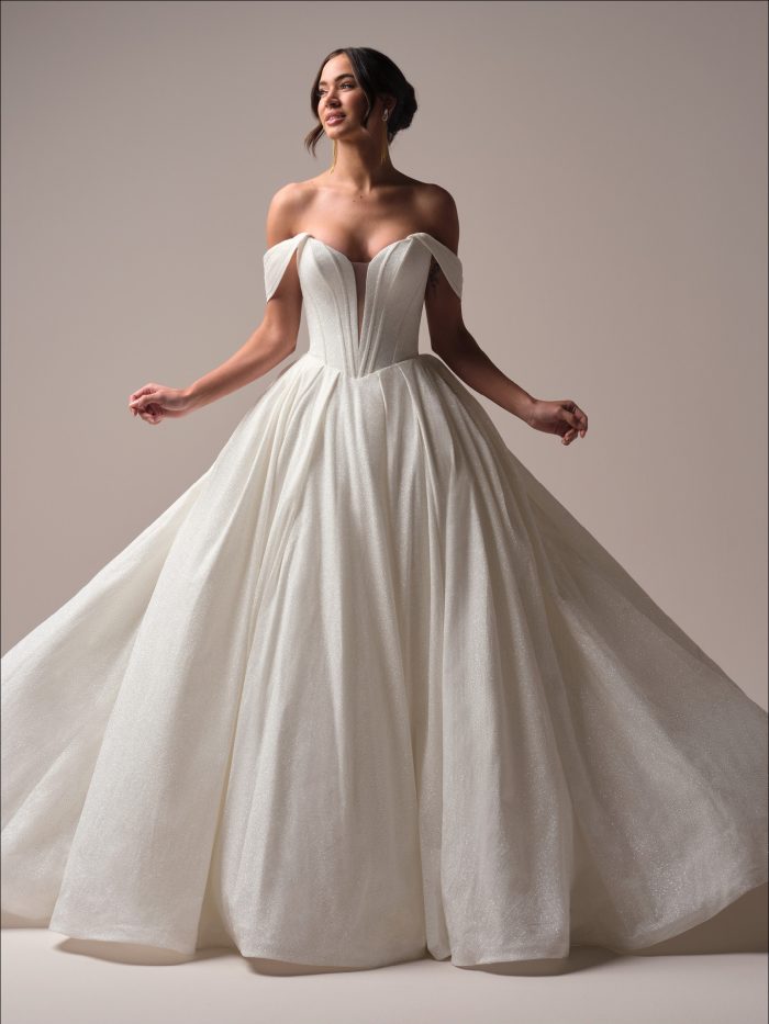 Bride wearing Derrick Royale ballgown wedding dress featuring glitter tulle, an exposed-boning bodice, and a soft basque waist. The gown has a plunging illusion V-neckline, off-the-shoulder straps, and a full shimmering skirt with pockets.