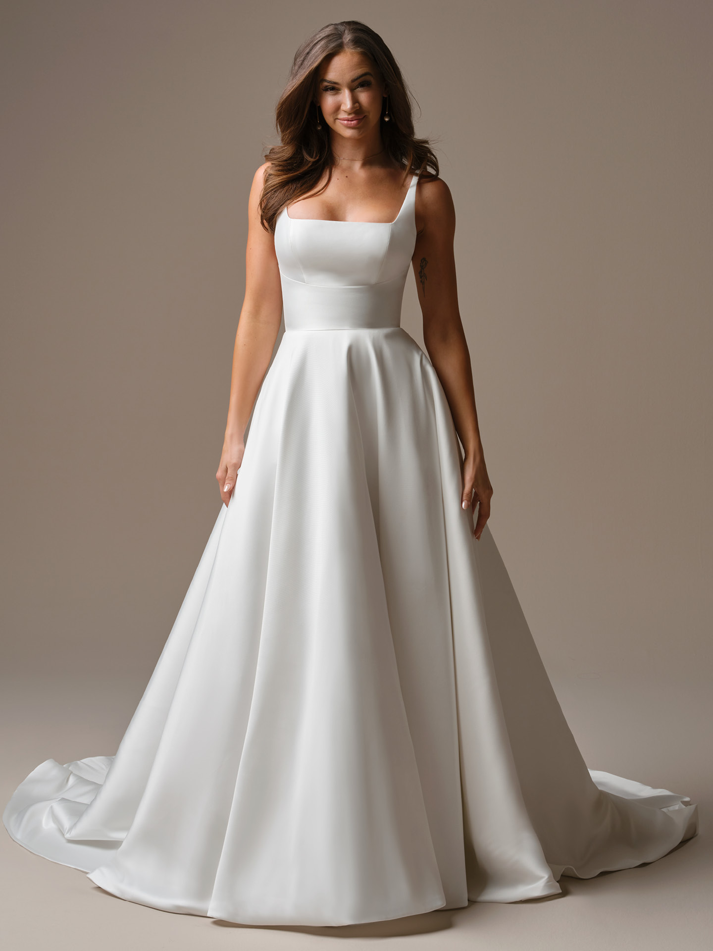 Bride wearing Galina by Maggie Sottero, a minimalist satin A-line wedding dress with a square neckline, wide straps, fitted bodice, and full flowing skirt with a soft train.