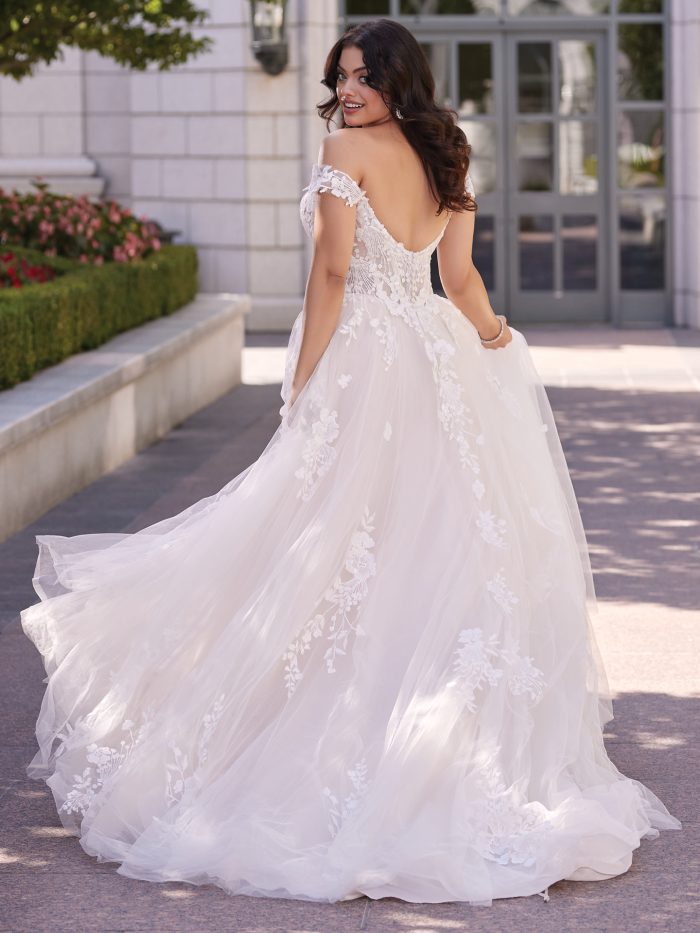 Back view of off-the-shoulder ball gown wedding dress featuring low scoop back, lace bodice, and flowing tulle skirt with floral appliqués trailing into a chapel-length train.