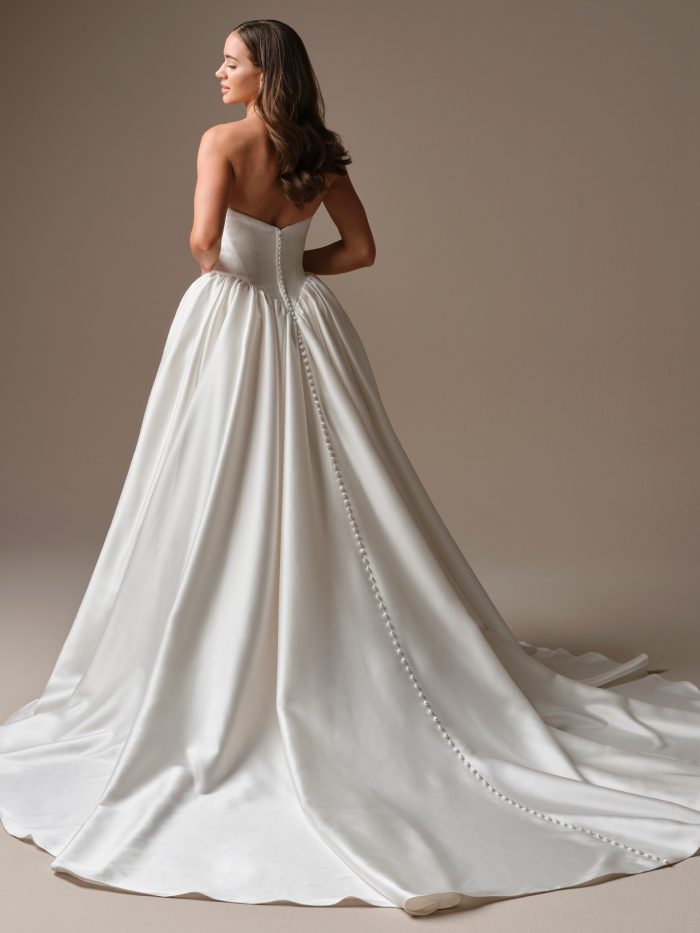 The back of a satin ball gown wedding dress featuring a clean strapless neckline, corset-inspired bodice, and a long row of covered buttons that trail from the waist down the sweeping train.