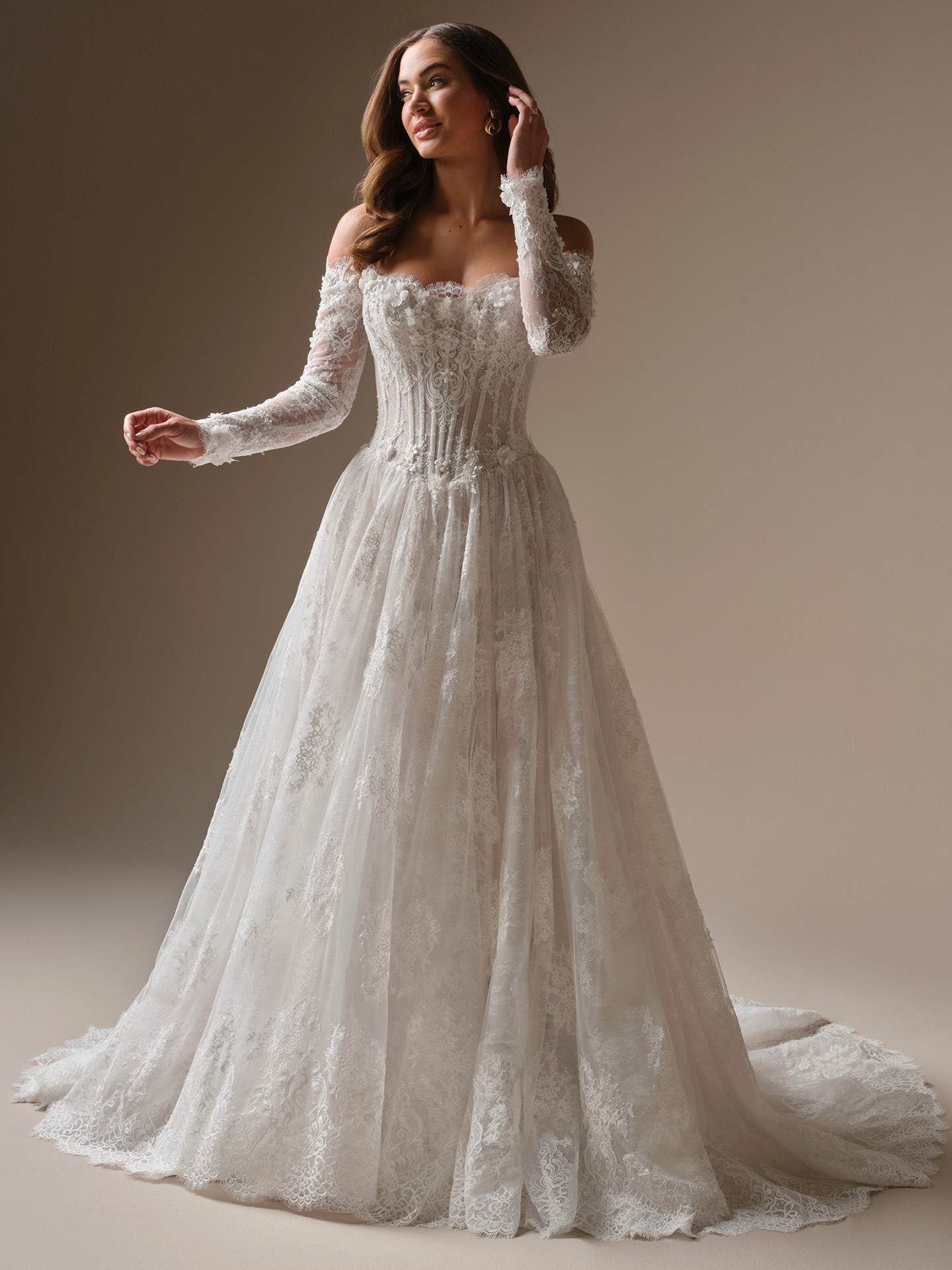 Bride wearing Kitaro by Maggie Sottero, an off-the-shoulder lace ballgown wedding dress with long illusion sleeves, a structured corset bodice, sweetheart neckline, and a full A-line skirt with lace appliqué and a sweeping train.