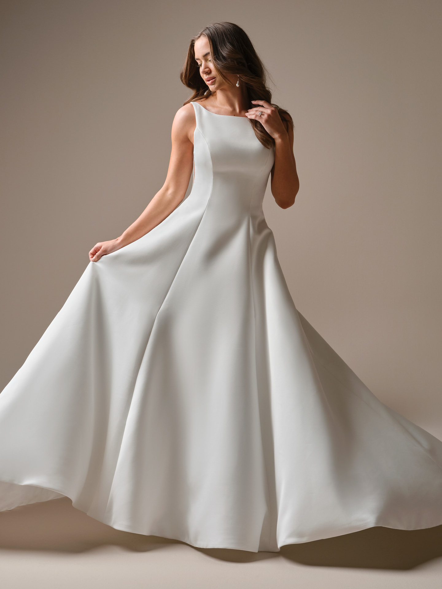 Bride wearing Lawrence by Maggie Sottero, a minimalist satin A-line wedding dress with a bateau neckline, fitted bodice, sculpted seam detailing, and a full flowing skirt with soft movement.