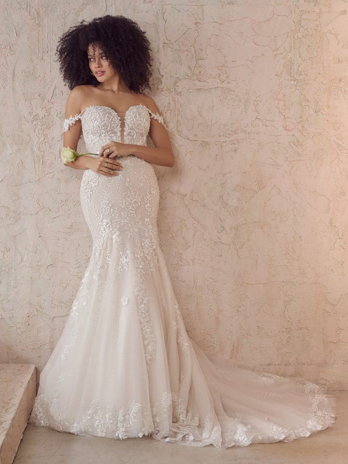 Bride wearing the Maggie Sottero Lennon fit-and-flare wedding dress featuring off-the-shoulder lace straps, a plunging illusion sweetheart neckline, and beaded lace motifs over glitter tulle with a soft, flowing train.