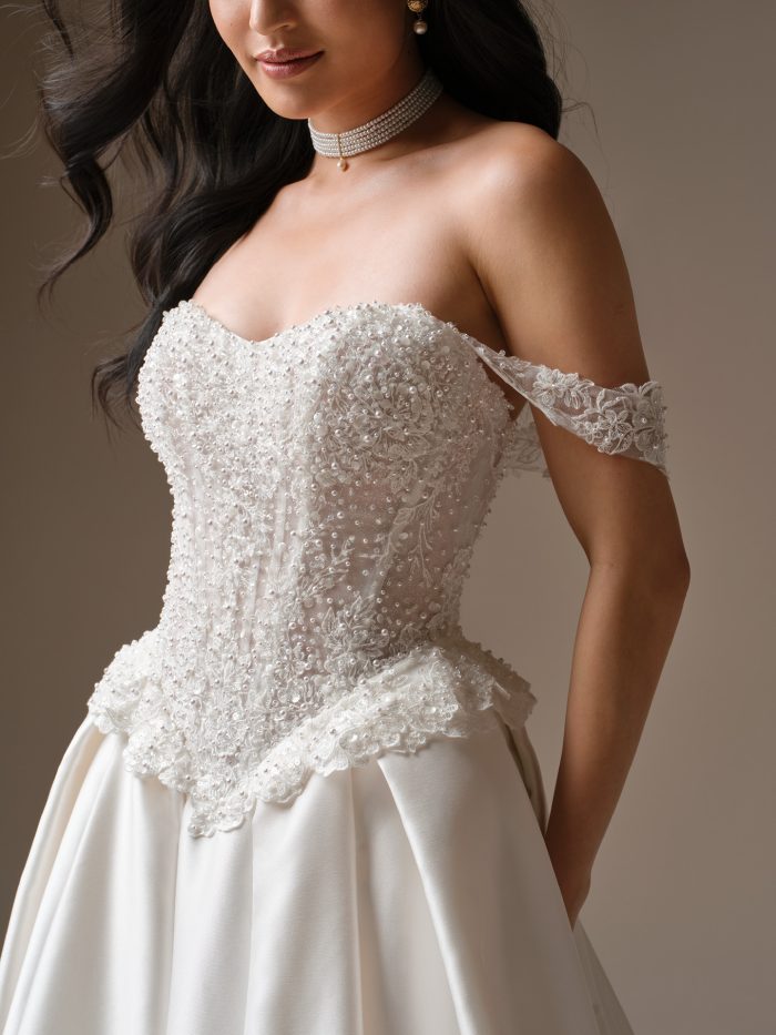 Close-up of Maggie Sottero London ballgown bodice with pearl and sequin beading, detachable off-the-shoulder lace straps, and basque waist detail.