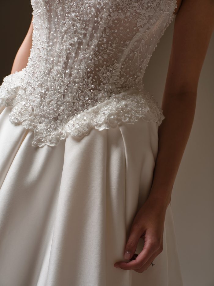 Close-up of the London ball gown wedding dress showing the intricately beaded corset bodice with pearl and lace detailing and the smooth satin skirt.