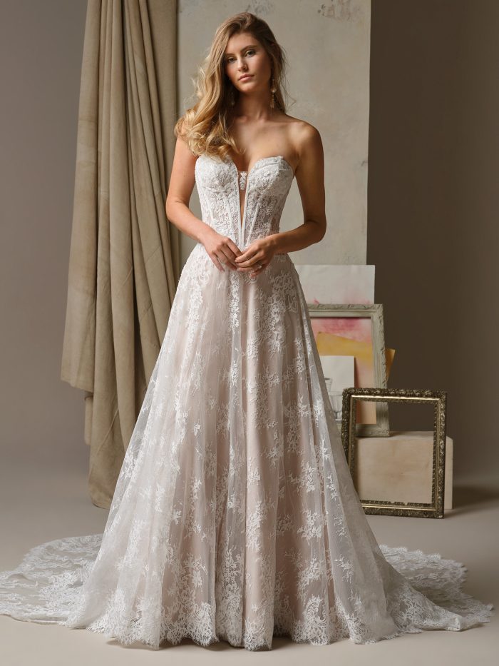 Image 1 Alt Text:
Bride wearing the Maggie Sottero Lucca A-line wedding dress featuring a strapless sweetheart neckline, sheer plunge detail, lace appliqué bodice, and soft blush tulle skirt with lace overlay and scalloped train.