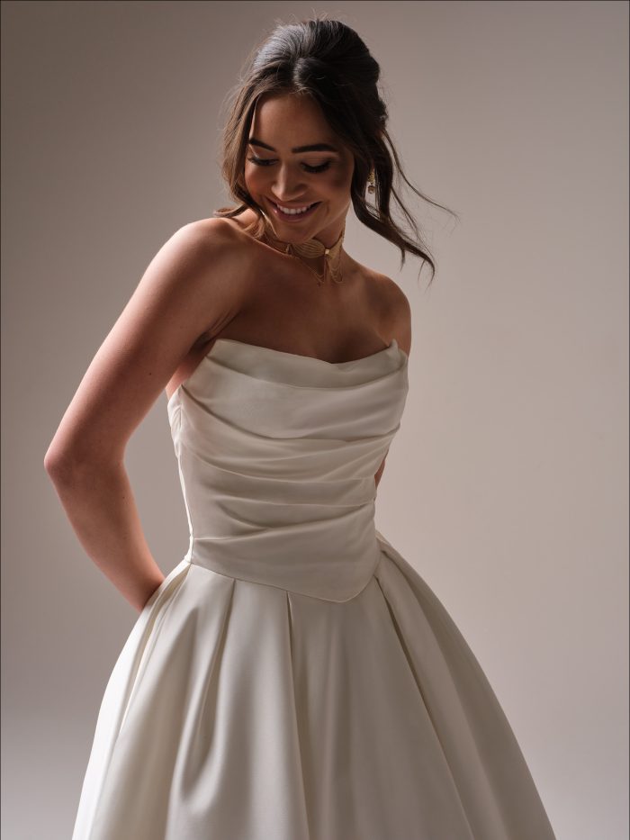 Close up of the Maureen wedding dress showing the softly draped satin bodice, strapless neckline, and pleated satin skirt.