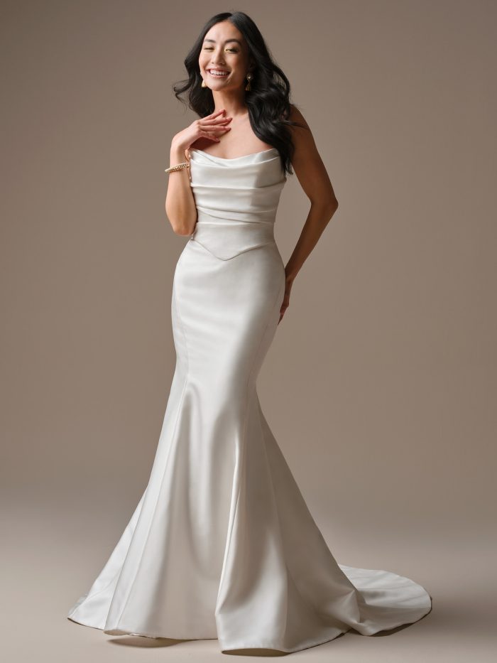 A model wearing the Maggie Sottero Maureen Lane wedding dress, featuring a sleek satin fit-and-flare silhouette with a draped neckline and smooth, fluid skirt.