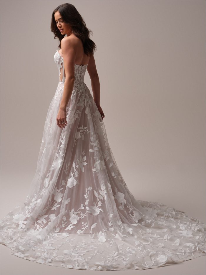 Back view of the Natalie gown showing the illusion lace train, corset-style back with covered buttons, and soft floral lace overlay flowing into a romantic chapel-length train.