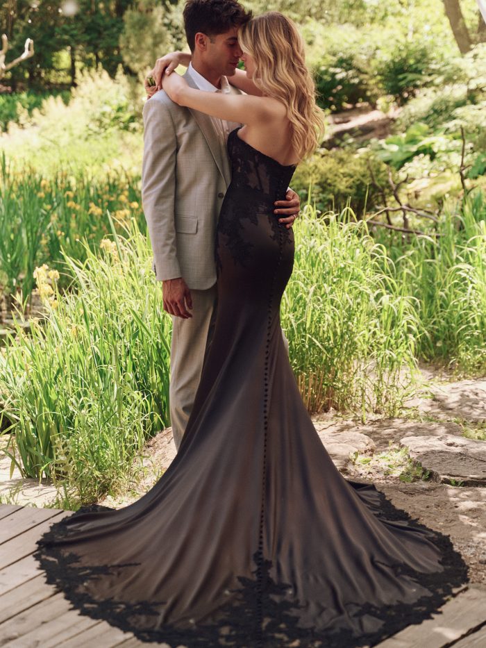 Back view of Persephone black sheath wedding dress by Maggie Sottero featuring illusion lace bodice, covered buttons, and chapel-length train with lace edging.