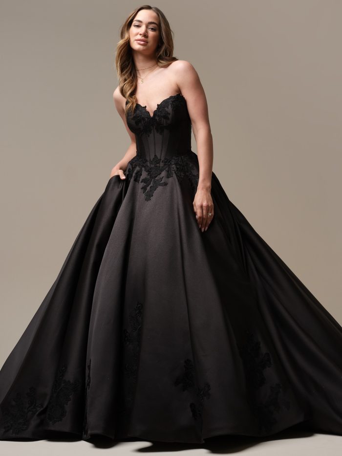Bride wearing a strapless black satin ball gown wedding dress with a sweetheart neckline, corset bodice, and lace appliqué detailing, posing gracefully in studio lighting.