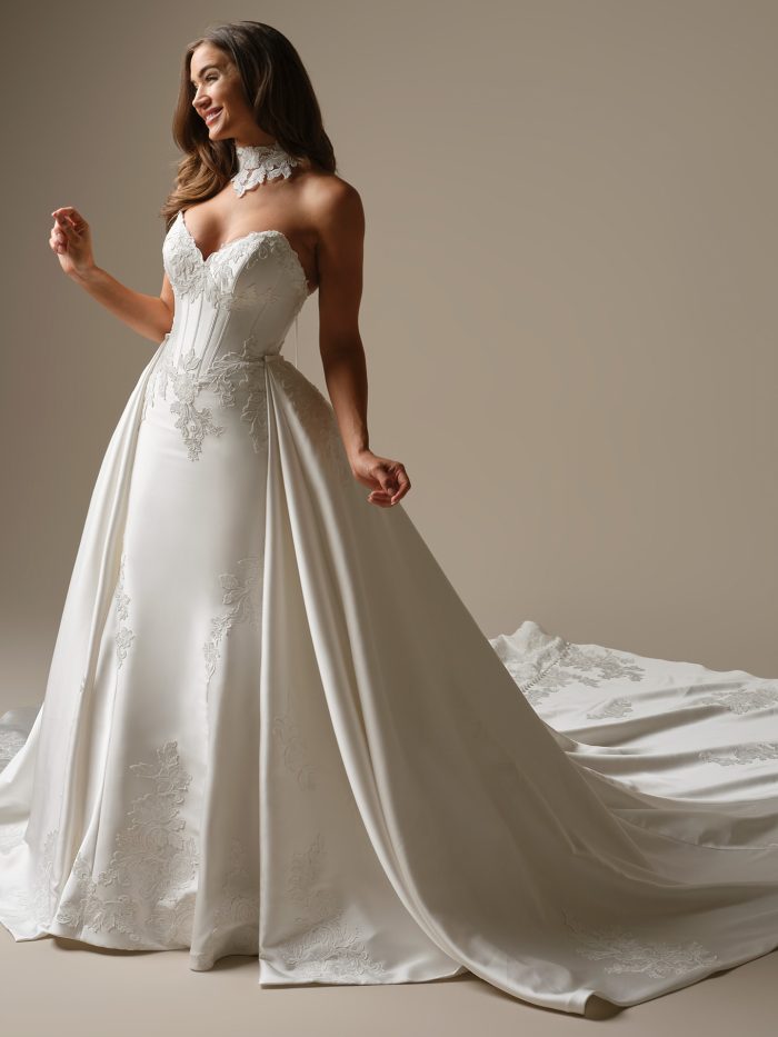 Bride wearing the Serafina Lane fit-and-flare wedding dress by Maggie Sottero featuring a strapless sweetheart neckline, structured corset bodice with lace appliqué, detachable choker collar, and a dramatic cathedral train.