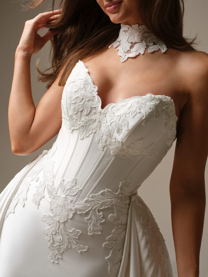 Close-up of the Serafina Lane wedding dress by Maggie Sottero highlighting the lace-appliqué corset bodice, sweetheart neckline, vertical boning, and detachable lace choker collar detail.
