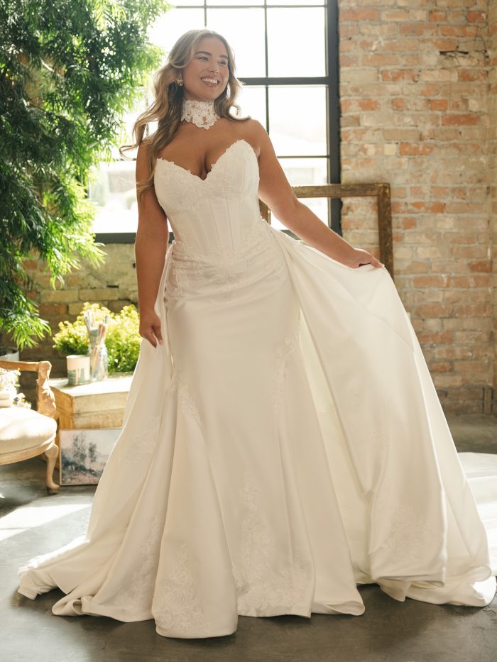 Bride wearing the Maggie Sottero Serafina Lane fit-and-flare wedding dress featuring a sweetheart neckline, corset-style bodice with lace appliqués, and detachable high-neck lace detail. The gown is styled with a flowing chapel-length train.