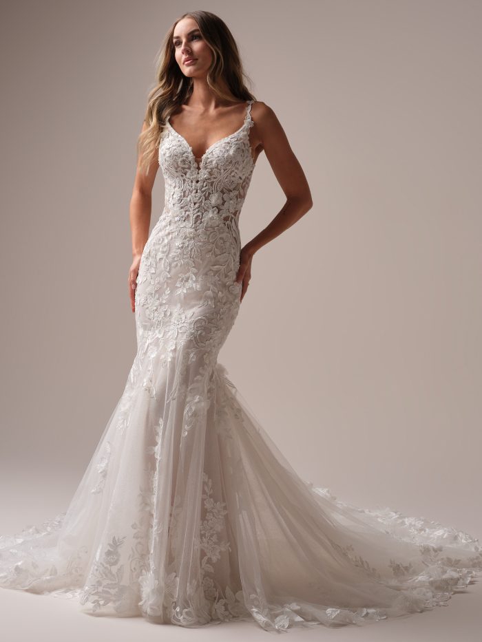 Bride wearing the Sonoma fit-and-flare wedding dress featuring allover lace, a plunging illusion V-neckline, delicate floral appliqués, and a low-back silhouette with a lace-trimmed train, photographed in a studio setting.