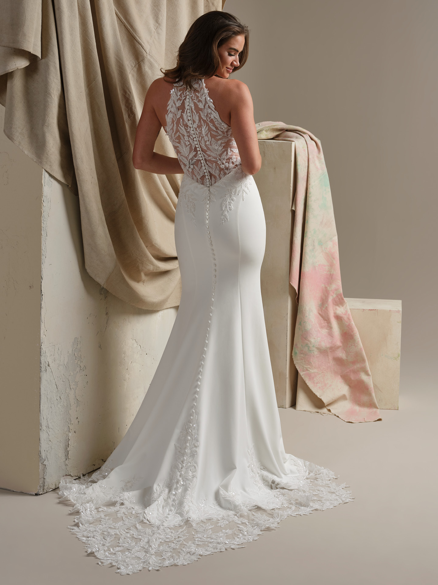 Back view of Spokane by Maggie Sottero featuring illusion lace halter back, covered button closure, fitted crepe skirt, and extended scalloped lace train.