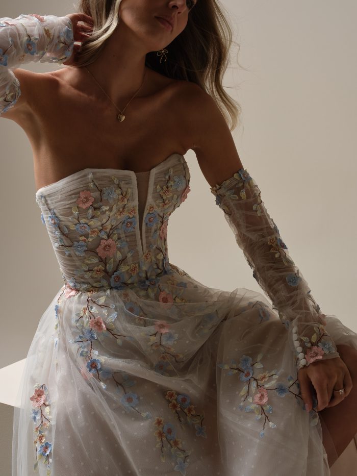 Close-up of the Maggie Sottero Zephyrine A-line wedding dress featuring a strapless corset bodice with sheer plunge detail, pastel floral embroidery, and matching sheer floral sleeves.