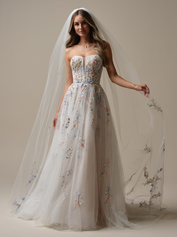 Bride wearing the Maggie Sottero Zephyrine A-line wedding dress with a strapless embroidered bodice, soft tulle skirt with pastel floral appliqués, and cathedral-length veil with coordinating floral details.