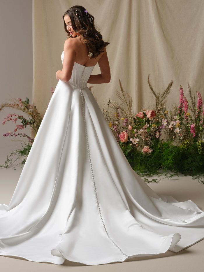 Alexia A-line wedding dress with a strapless corset bodice, satin button down train, and full satin skirt captured in a floral studio setting.