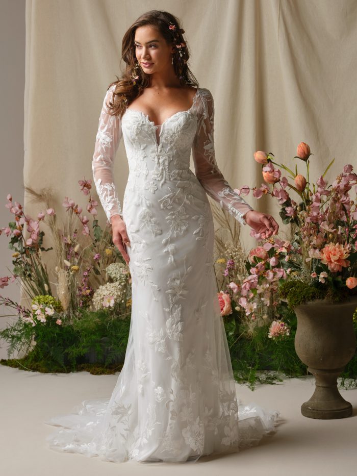 Rebecca Ingram Aubra sheath wedding dress featuring a sweetheart neckline, illusion long sleeves, and floral lace appliqués over soft tulle with a fitted silhouette.