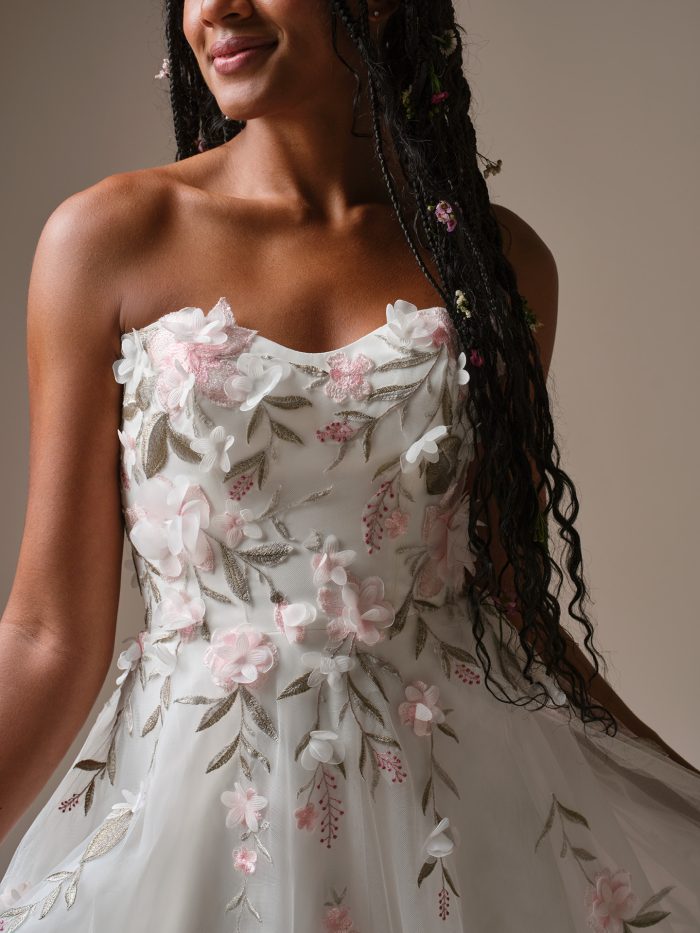Close-up of the Blossom boho wedding dress featuring a strapless bodice with pastel floral embroidery, dimensional appliqués, and airy tulle fabric.