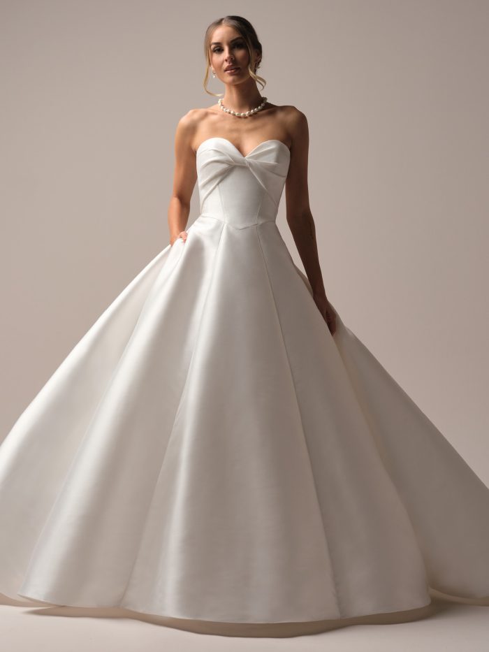 Bride wearing a strapless satin ball gown wedding dress with a twisted sweetheart neckline and structured bodice, styled with pearl jewelry and soft updo.