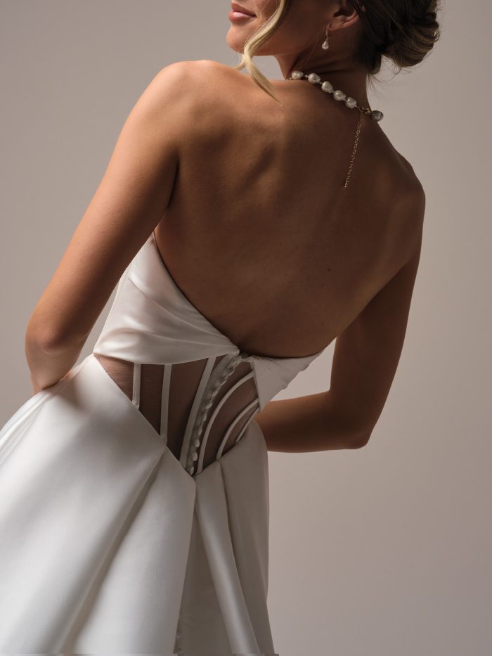 Back view of a strapless satin ball gown wedding dress featuring illusion corset details and covered buttons, highlighting the modern back design and smooth train.