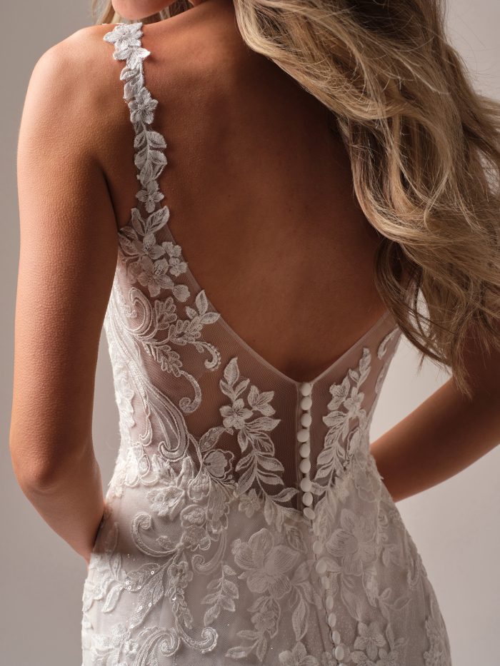 Back view of the Rebecca Ingram Candice sheath wedding dress showing illusion lace straps, low V-back with covered buttons, and embroidered lace appliqués with subtle shimmer.