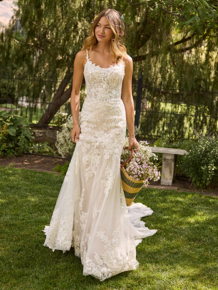 Bride wearing a fit-and-flare lace wedding dress with illusion straps and a scoop neckline. The gown features floral lace appliqués, sequin detailing, and a chapel-length train, styled for a soft and romantic garden bridal look.