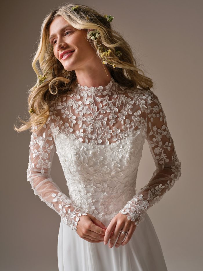 Georgina by Rebecca Ingram wedding dress featuring illusion lace high neckline, long sheer sleeves, and soft A-line skirt, close-up detail