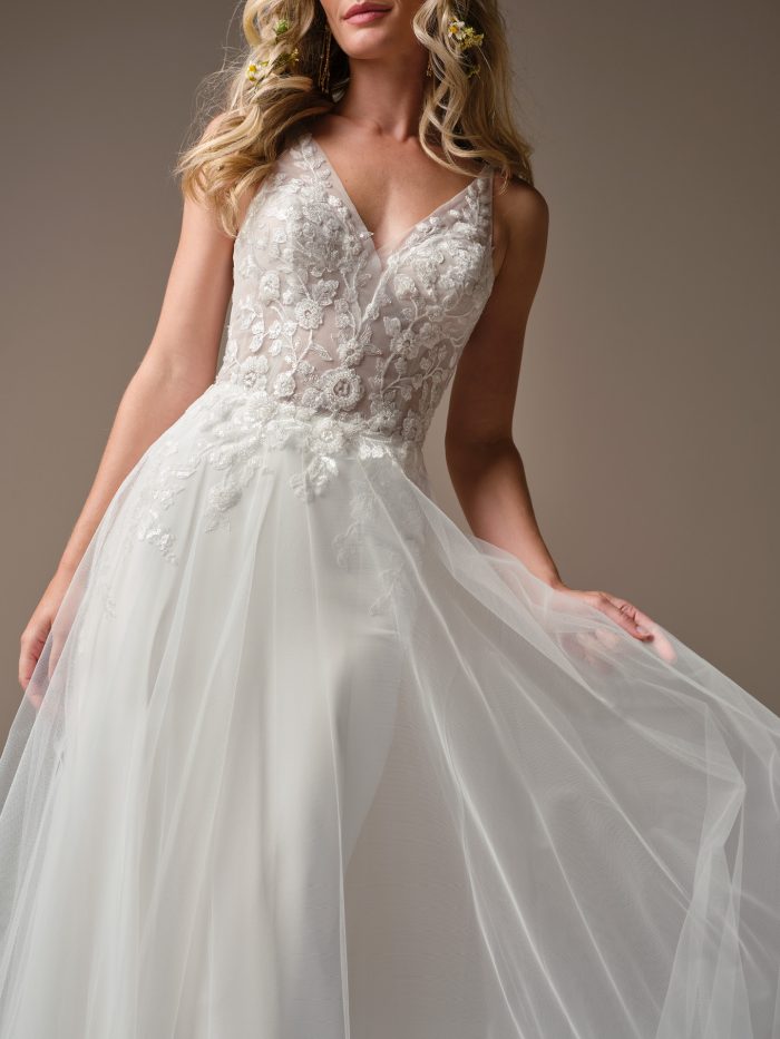 Close-up of the Rebecca Ingram Holly wedding dress featuring a beaded illusion lace bodice, plunging V-neckline, and soft tulle skirt overlay.