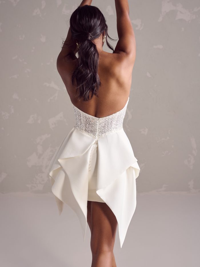 Back view of the Jackie short wedding dress showing the strapless beaded bodice, button closure, and dramatic layered satin skirt with sculptural folds.