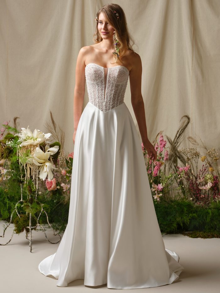 Full-length view of the Marty A-line wedding dress by Rebecca Ingram featuring a strapless sweetheart neckline, beaded corset bodice with subtle plunge detail, and a flowing satin skirt with pockets.