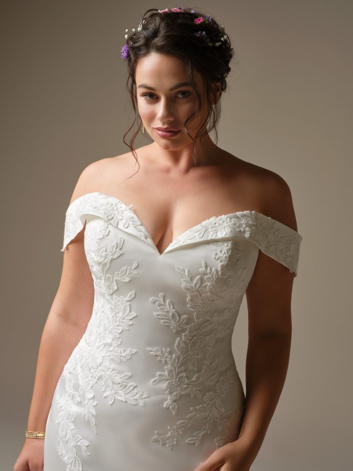 A close-up of the Rebecca Ingram Miley wedding dress showing the off-the-shoulder neckline, embroidered lace motifs and fitted bodice