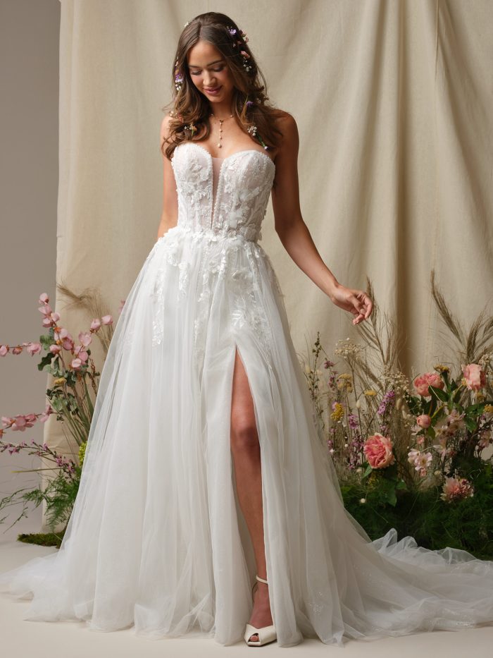 Nora A-line wedding dress featuring a strapless sweetheart neckline, 3D floral lace bodice, thigh high skirt slit, and soft layered tulle in a floral studio setting.