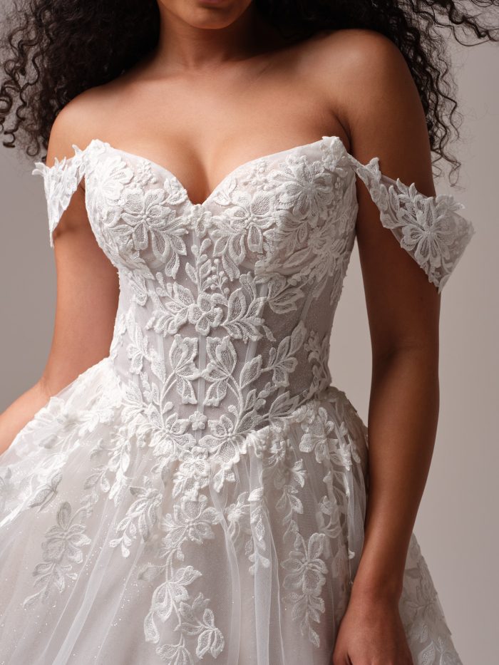 Close-up of floral lace off-the-shoulder wedding dress featuring a sweetheart neckline, structured bodice, and delicate embroidered appliqués on tulle.