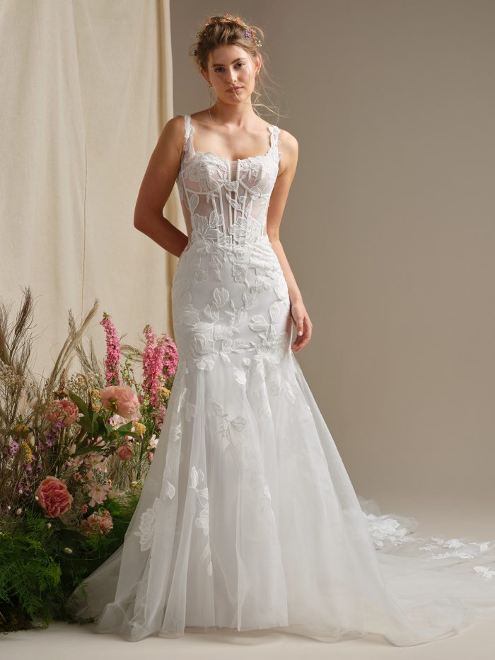 Bride wearing Pearline by Rebecca Ingram, a fit-and-flare lace wedding dress with illusion straps, a square neckline, and sheer corset bodice adorned with floral lace motifs.