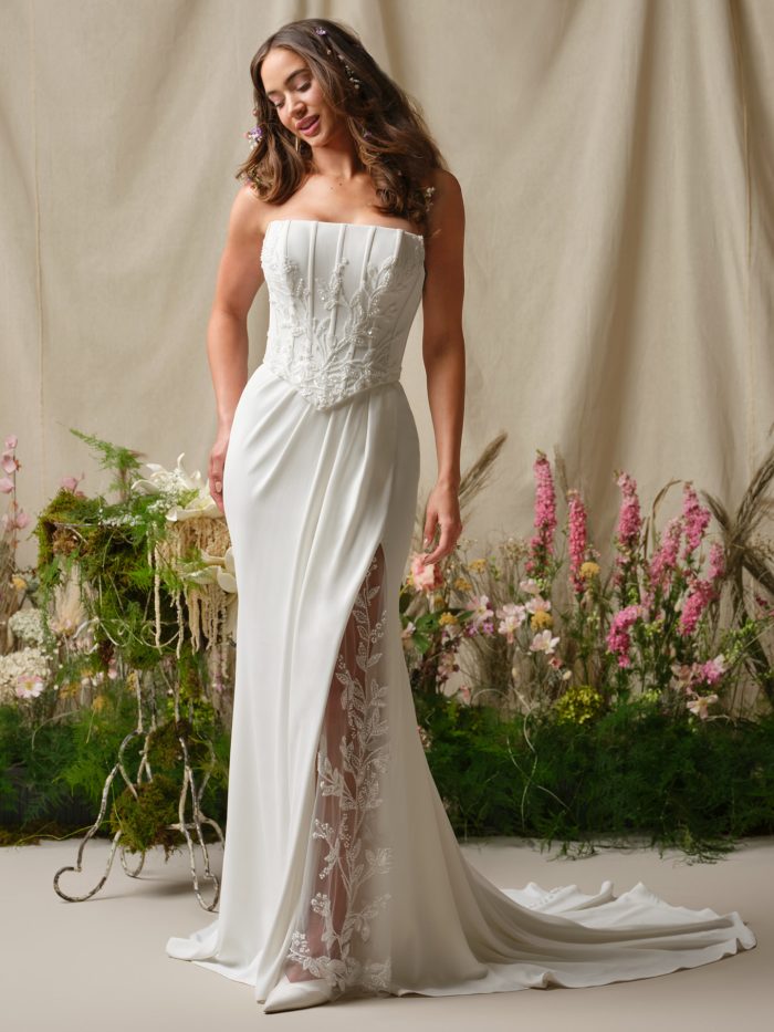 Front view of Rebecca Ingram Terry sheath wedding dress featuring a strapless straight neckline, beaded lace corset bodice, and illusion lace slit over crepe skirt.