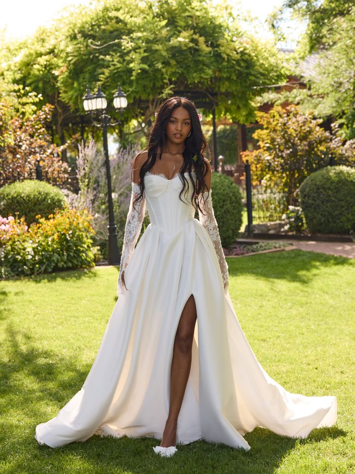 Bride wearing Zorina by Rebecca Ingram, an ivory gown with a side slit and peakaboo lace sweetheart neckline, while walking through a garden