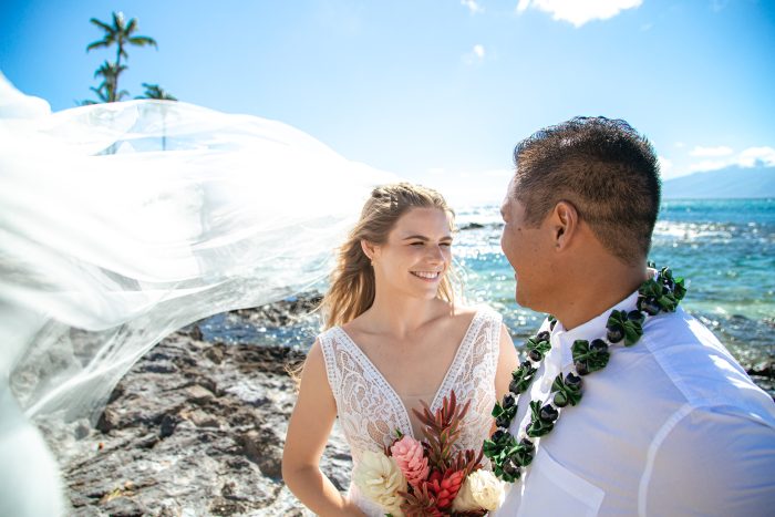 Bride Looking at Groom with Veil Blowing in the Wind on the Beach
