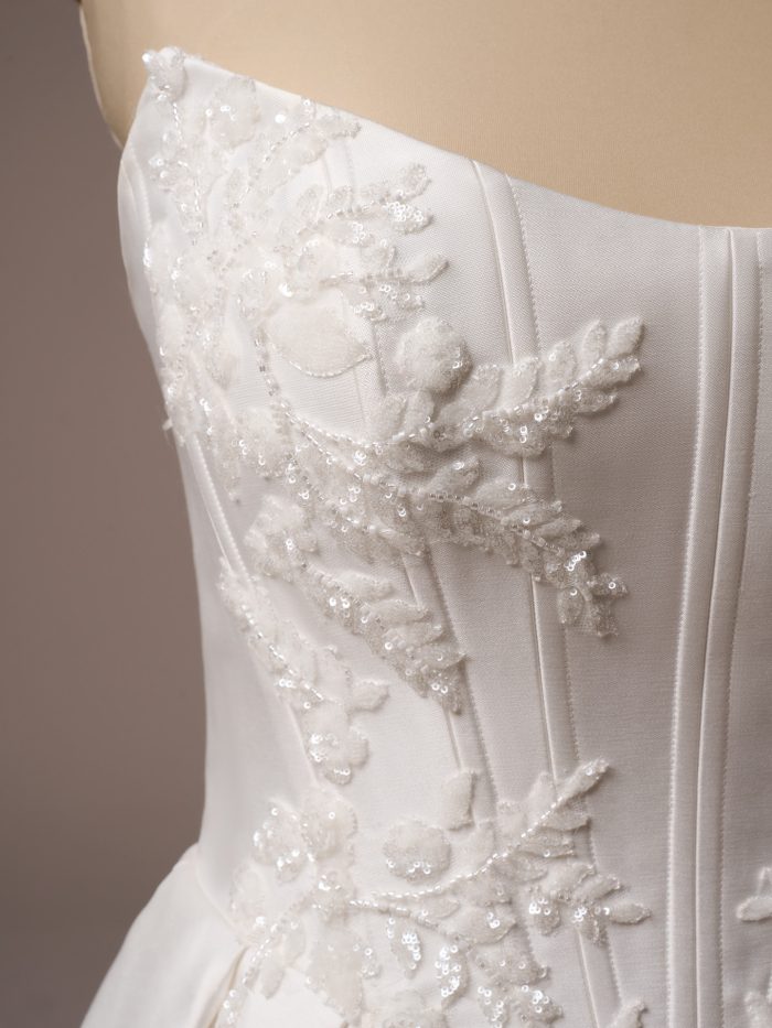 Close-up of the Sottero and Midgley Amadora wedding dress showing intricate beaded lace appliqués with sequins embroidered on the structured satin bodice.